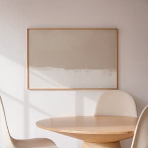 May include: A light beige abstract painting in a wooden frame hangs on a white wall above a round wooden table with two white chairs.