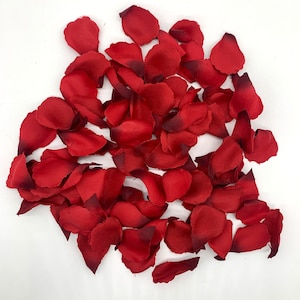 May include: A pile of red rose petals, scattered on a white background. The petals are soft and velvety, with a slight sheen.