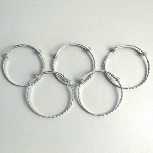 May include: Five silver adjustable bangle bracelets. Each bracelet features a twisted rope design around the band and a simple clasp. The bracelets are arranged on a white surface.