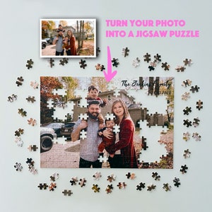 May include: A custom jigsaw puzzle featuring a family of four standing in front of a house. The puzzle is partially assembled and the pieces are scattered around the puzzle. The text "The Jenkins Family 28.03.2023" is printed on the puzzle.