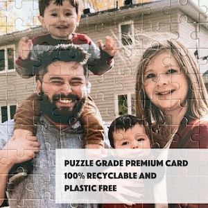 May include: A family portrait featuring a man, a woman, and two young children. The man is holding one child on his shoulders, while the other child is standing in front of him. The family is smiling and looking at the camera. The image is printed on a puzzle grade premium card, 100% recyclable and plastic free.