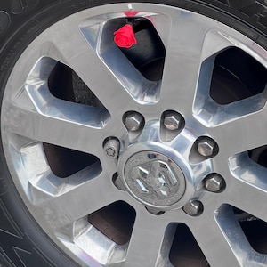 May include: Close-up of a shiny chrome truck wheel with a red rose valve stem cap. The wheel has a silver center cap with the Ram logo and black tire. The tire is a Goodyear.