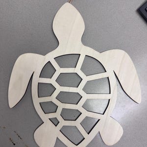 May include: A wooden cutout of a sea turtle with a detailed shell design. The turtle is unpainted and ready for crafting.