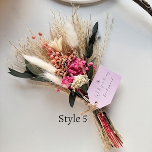 May include: A dried flower bouquet featuring pink, white, and beige flowers, with green leaves and wheat-like stems. A pink tag tied to the bouquet reads "Will you be my bridesmaid." The text "Style 5" is below the bouquet.
