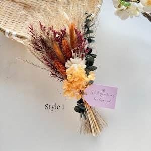 May include: A dried flower bouquet featuring a mix of textures and colors, including orange, burgundy, and cream. The bouquet is tied with natural twine and includes a tag that reads "Will you be my bridesmaid". The text "Style 1" is also visible.
