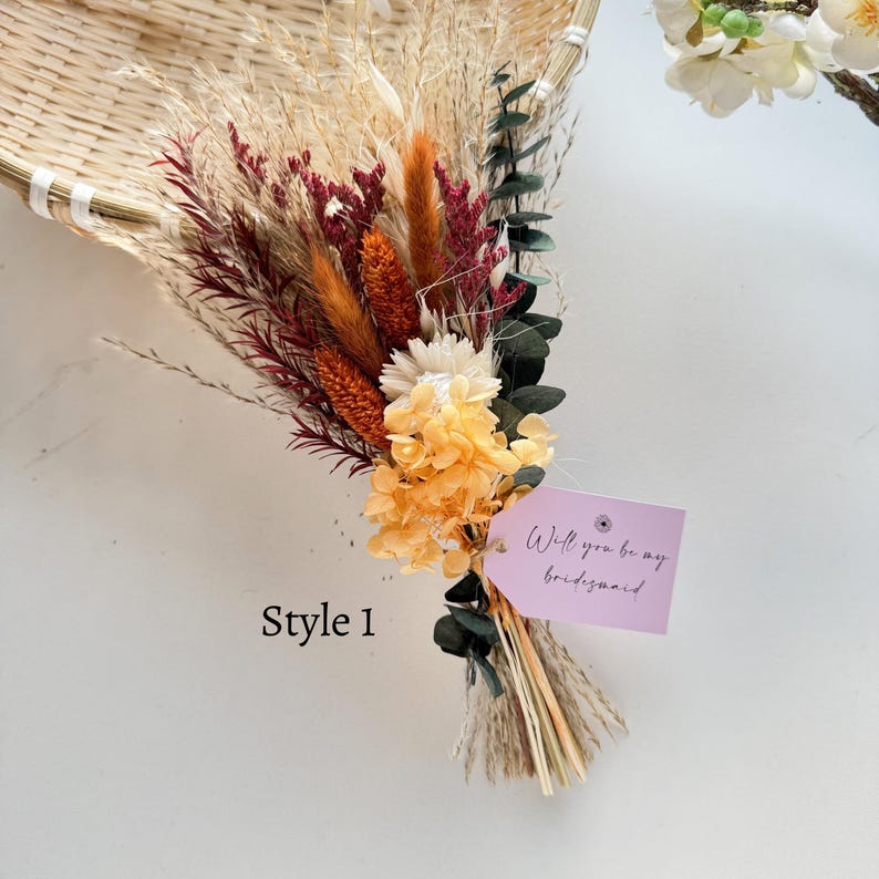 May include: A dried flower bouquet featuring a mix of textures and colors, including orange, burgundy, and cream. The bouquet is tied with natural twine and includes a tag that reads "Will you be my bridesmaid". The text "Style 1" is also visible.