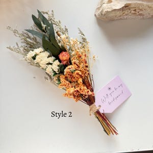May include: A dried flower bouquet featuring a mix of orange, cream, and green foliage, tied with twine. A pink tag reads "Will you be my bridesmaid." The text "Style 2" is also visible.