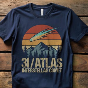 May include: Navy blue t-shirt with a retro design depicting a comet, mountains, and a sunset. The text reads "3I/ATLAS Interstellar Comet" in a vintage font. A stylish tee for space enthusiasts.