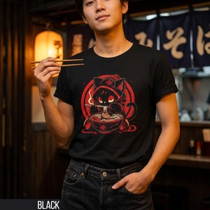 May include: Black t-shirt featuring a red and black graphic of a cat wearing a hat and eating ramen from a bowl. The cat is inside a red circle. The word "BLACK" is at the bottom of the image.