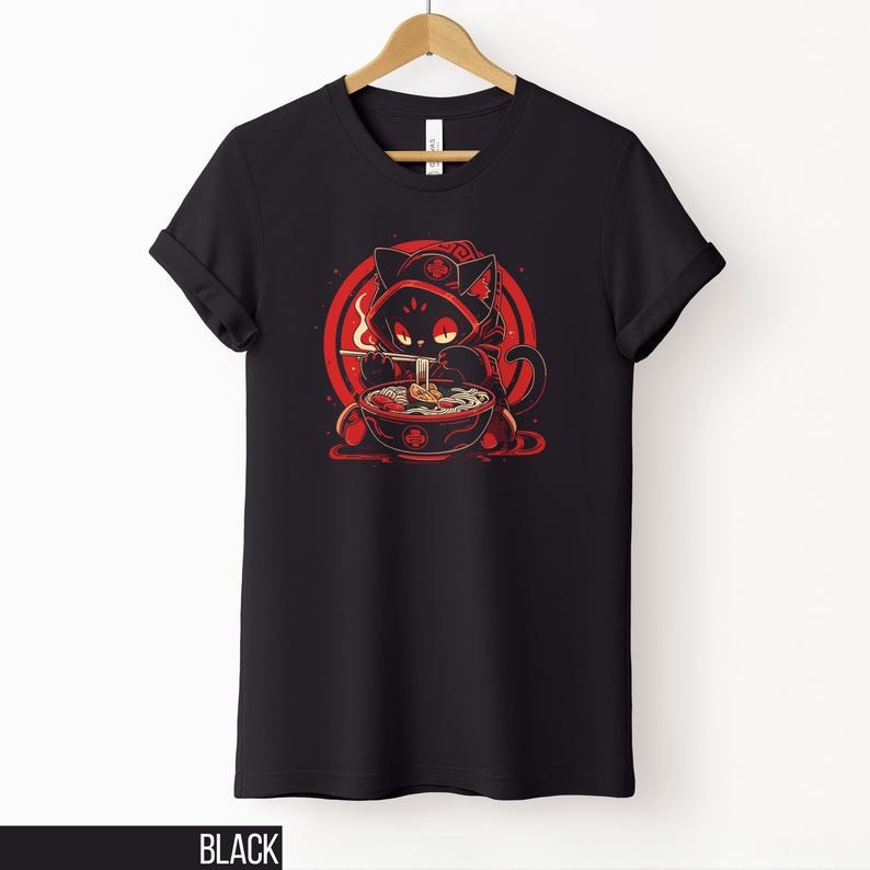 May include: Black t-shirt featuring a cartoon cat in a red hooded cloak, eating ramen from a bowl. The graphic is set against a red circular background. The word "BLACK" is printed at the bottom of the shirt.