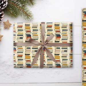 May include: A gift wrapped in brown paper with a book stack pattern. The paper is cream colored with stacks of colorful books printed on it. The gift is tied with a brown ribbon.