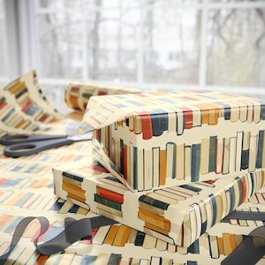 May include: A stack of gift boxes wrapped in brown paper with a colorful book print. The boxes are wrapped in a pattern of books with different colors and sizes. The boxes are sitting on a table with a white background.