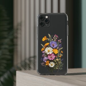 May include: A clear phone case with a bouquet of pressed flowers in shades of purple, pink, yellow, and white. The flowers are arranged in a loose, natural style.