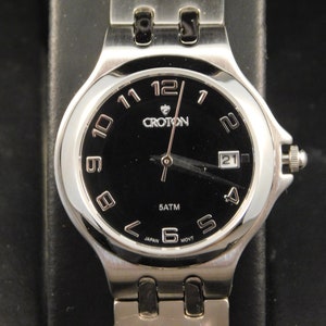 May include: A silver Croton wristwatch with a black face and silver hands. The watch has a date window at the 3 o'clock position and says "5 ATM" and "JAPAN MOV'T" on the face.