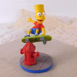 May include: A Bart Simpson figurine skateboarding over a red fire hydrant. Bart wears a red top, blue shorts, and yellow hair. The skateboard is green. The base is a blue circle with a grey pavement design.