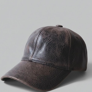 May include: A brown leather baseball cap with a curved peak. The cap has a textured surface and a small button on top. The colour is a dark, distressed brown.