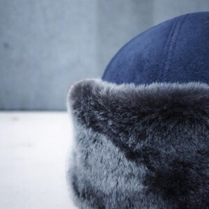 May include: A close-up of a navy blue hat with a faux fur trim. The hat has a rounded crown and a soft, textured appearance. The fur trim is a dark gray color.