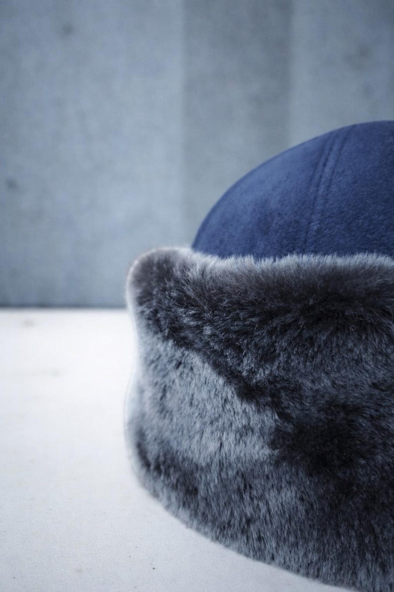 May include: A close-up of a navy blue hat with a faux fur trim. The hat has a rounded crown and a soft, textured appearance. The fur trim is a dark gray color.