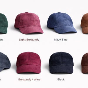 Puede incluir: Colección de ocho gorras de béisbol de ante en varios colores, incluyendo verde oscuro, burdeos claro, azul marino y camel. Cada gorra se muestra con su nombre de color debajo.