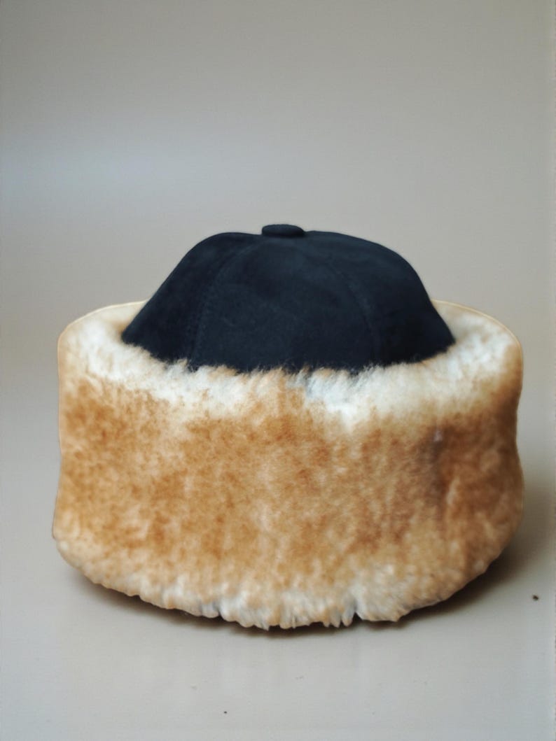 May include: A black hat with a rounded crown and a fluffy, tan-colored fur trim. The hat appears to be made of a soft material and is designed to keep the wearer warm. The fur trim is thick and plush.