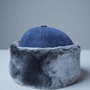 May include: A blue winter hat with a faux fur trim. The hat features a rounded crown and a soft, plush fur band around the base. The hat is designed to provide warmth and protection from the cold.