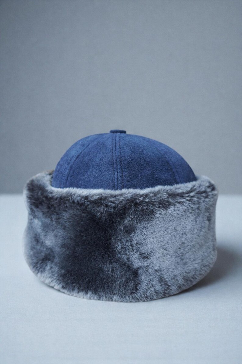 May include: A blue winter hat with a faux fur trim. The hat features a rounded crown and a soft, plush fur band around the base. The hat is designed to provide warmth and protection from the cold.