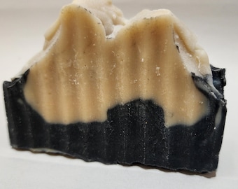 Peut inclure: Un pain de savon artisanal avec un design en couches. La couche inférieure est noire, le milieu est beige et le dessus est blanc crème. Le savon a une surface texturée et un aspect naturel et organique. Ce savon est probablement pour l'hygiène personnelle.