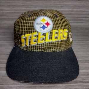 May include: A black and yellow baseball cap with a Pittsburgh Steelers logo and the word "Steelers" embroidered on the front.
