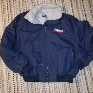 May include: A navy blue jacket with a fleece lining and a zipper closure. The jacket has a logo on the front that says "PRIMUS".