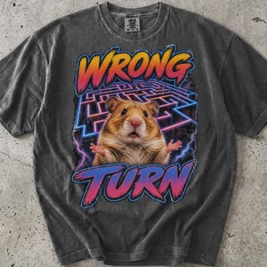 May include: A charcoal grey short-sleeve t-shirt featuring a graphic print of a hamster centered in a neon blue maze. The text WRONG TURN is printed in a pink and orange gradient font above and below the hamster. The word PEPPER is at the top.
