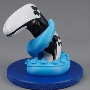 Può includere: Un controller per videogiochi bianco e nero sostenuto da un supporto a forma di tentacolo di polpo blu brillante. Il tentacolo presenta ventose visibili ed è montato su una base circolare blu scuro con un bordo zigrinato e testurizzato.