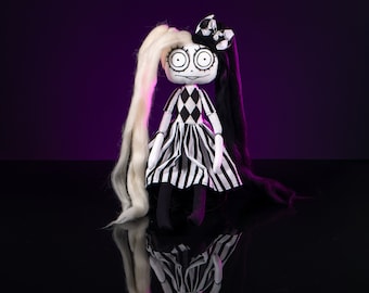 May include: A black and white doll with long black and white hair, wearing a black and white checkered dress with a black bow. The doll has large eyes and a wide smile. The doll is sitting on a black surface with a purple background.
