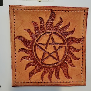 Peut inclure: Patch carré en cuir beige avec une bordure cousue. Le motif représente un soleil rouge foncé entourant une étoile à cinq branches. Le cuir a un aspect texturé.