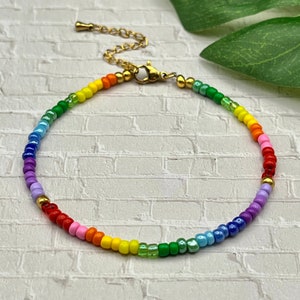 May include: A rainbow beaded bracelet with a gold clasp. The bracelet is made with small, colorful beads in a rainbow pattern.