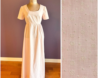May include: A floor-length light pink dress with short sleeves and a scoop neckline. The fabric features a subtle, tonal embroidered pattern of small flowers and dots throughout, visible in the detailed close-up view of the textile.