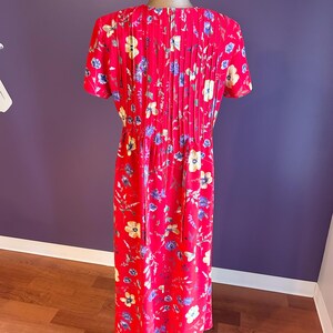 May include: A red floral print dress with short sleeves and a pleated back. The dress features a pattern of yellow, blue, and white flowers. The dress is displayed on a mannequin.