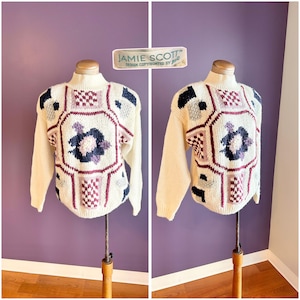 May include: Cream-colored sweater with a geometric design featuring burgundy, navy, and purple accents. The sweater has a high neck and long sleeves. The tag reads "JAMIE SCOTT DESIGN COPYRIGHTED BY JESS".