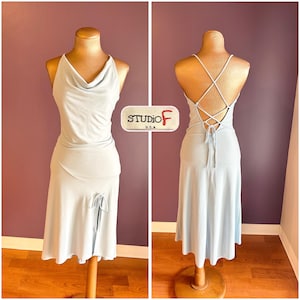 May include: A pale blue dress with a cowl neck and a split skirt, shown on a mannequin. The back of the dress has crisscross straps and a tie. The label reads "STUDIO F U.S.A."