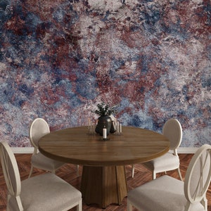 May include: A round wooden dining table with a pedestal base surrounded by four upholstered chairs with light beige fabric. A dark vase with greenery and several lit candles sit on the table against a textured wall with blue and red tones.