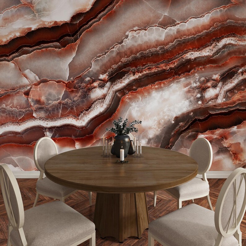 May include: A round wooden dining table with a central pedestal base surrounded by four upholstered chairs with oval backs. The background features a large-scale wall mural displaying a polished red and white marble stone texture with veins.