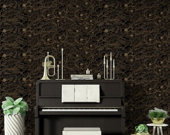 May include: A black grand piano with a gold trim sits in front of a black and gold floral wallpaper. The piano has a white piano bench and a book on top of it.