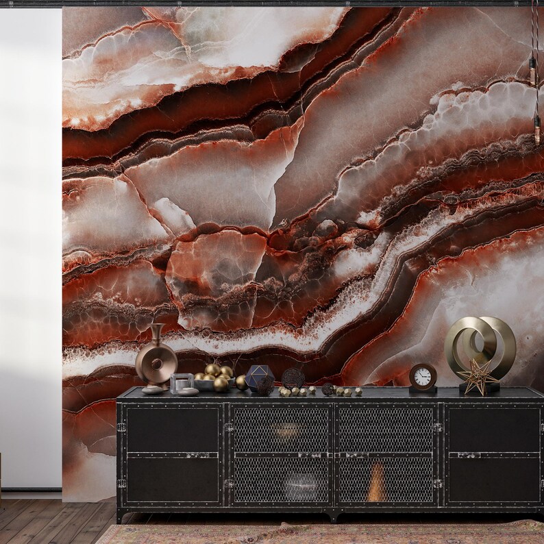 May include: A black metal sideboard with mesh cabinet doors sits against a wall featuring a large-scale mural of brown, white, and deep red agate stone patterns. Decorative objects including a clock and metallic sculptures rest on the top surface.