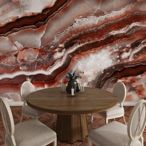 May include: A round wooden dining table with a central pedestal base surrounded by four upholstered chairs with oval backs. The background features a large-scale wall mural displaying a polished red and white marble stone texture with veins.