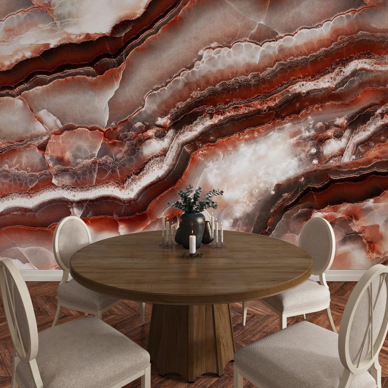 May include: A round wooden dining table with a central pedestal base surrounded by four upholstered chairs with oval backs. The background features a large-scale wall mural displaying a polished red and white marble stone texture with veins.