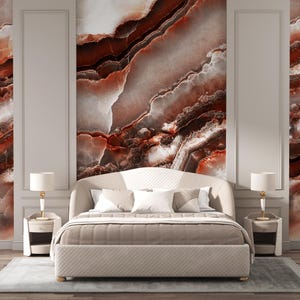 May include: A beige upholstered bed with a curved headboard featuring a quilted pattern, positioned between two matching beige nightstands. Each nightstand holds a white lamp with a gold base. The wall behind the bed displays a large marble mural.