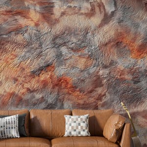 May include: A tan leather sofa featuring three cushions and two decorative pillows, one with a geometric triangle pattern and one with a checkered pattern, positioned against a textured wall mural with swirling shades of rust, gray, and brown.
