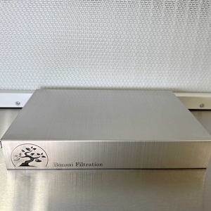 May include: A silver metal box with a brushed finish. The box has a logo of a bonsai tree and the text "Bonsai Filtration" on the front.
