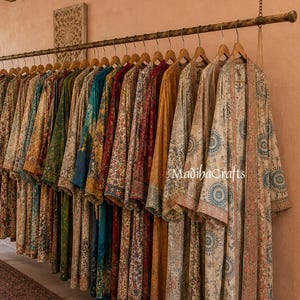 May include: A row of long, open-front robes hanging on a metal rack, featuring various floral and geometric patterns in colors including blue, red, yellow, and green. The text MadibaCrafts is visible on the rightmost robe in the collection.