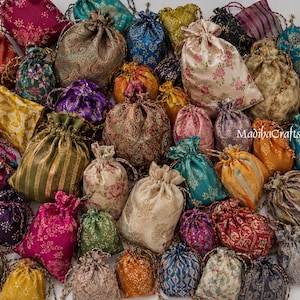 Può includere: Una collezione di numerose piccole borse con coulisse realizzate in vari tessuti con motivi, colori e texture diversi, inclusi disegni floreali, paisley e geometrici, con il testo MadibaCrafts visibile su una delle borse.