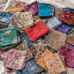 May include: A large collection of square fabric swatches featuring diverse floral and geometric patterns in vibrant colors including red, blue, green, yellow, and purple. The fabric pieces are stacked in a pile with the text MadibaCrafts visible.